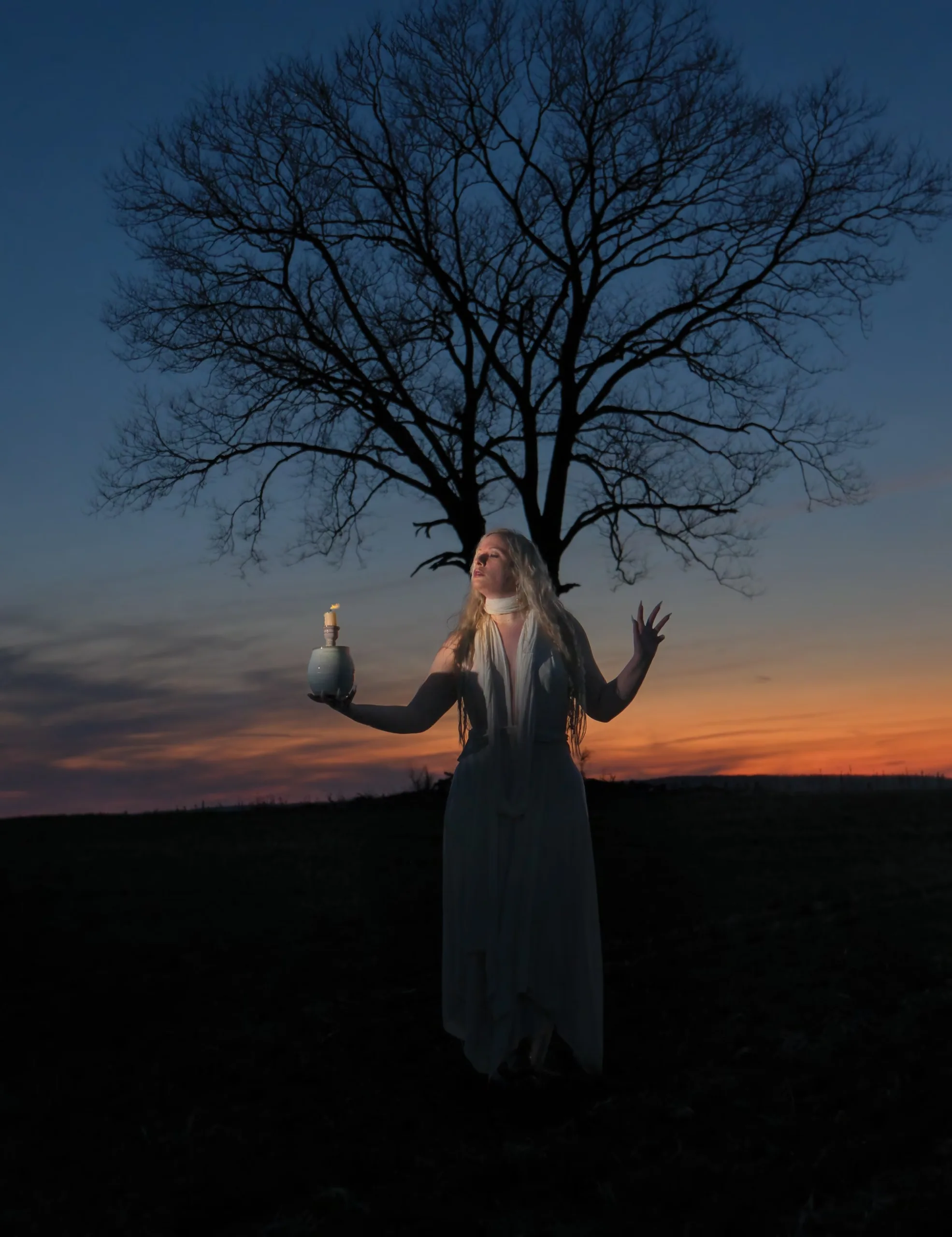 Winter Enchantment: Ceramicist Rachael Platt holding a lit manifesting jar under the full moon, surrounded by illuminated jars in a forest setting. Photography by steve parke